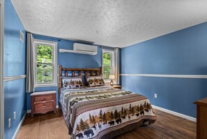 A bedroom with a large bed, two windows, a nightstand, and a wooden headboard. - Smoky Everest 4 Bedroom Chalet (Newport)