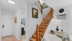 A staircase with wooden railings leading to an upper floor, a white door, and a wall-mounted clock.