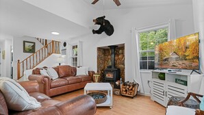 A cozy living room with a leather sofa, a stone fireplace, a bear mounted on the wall, and a television displaying autumn leaves.