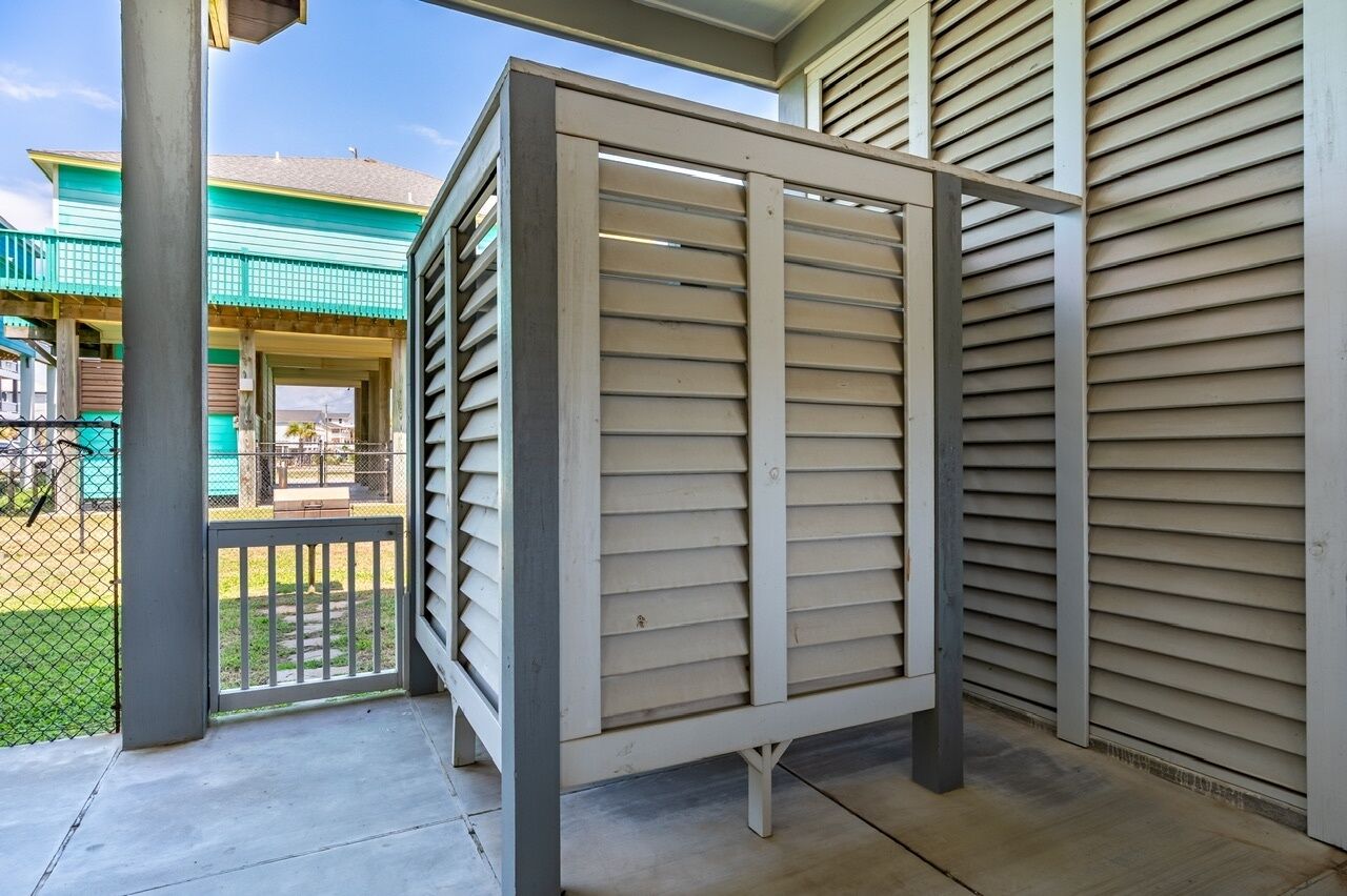 Un espacio al aire libre techado con una reja metálica, suelo de hormigón y vistas a una casa con techo verde y porche.
