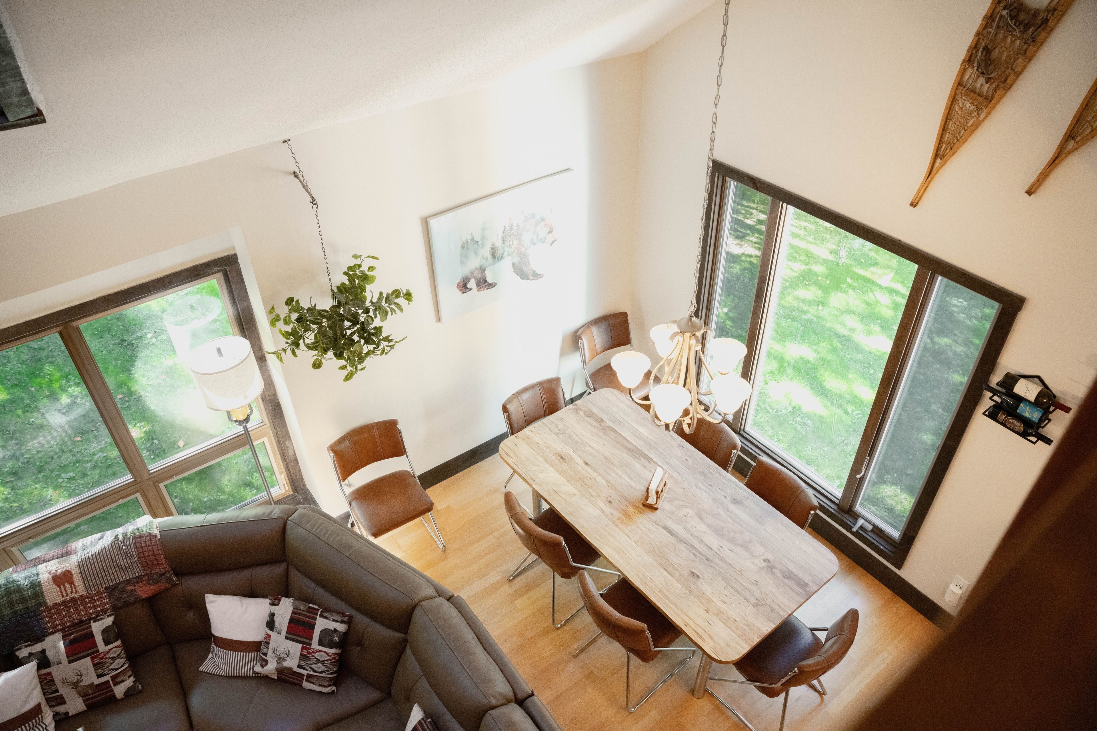 Een moderne eethoek met een houten tafel en stoelen, grote ramen en uitzicht op groen buiten.