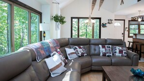 A modern living room with a sectional sofa, large windows, and a view of trees.