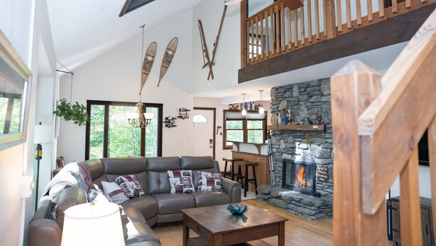 A spacious living room with a large sectional sofa, a fireplace, and a wooden ceiling fan.