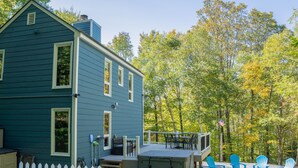 A blue house with a deck, outdoor seating, and a view of a forest.