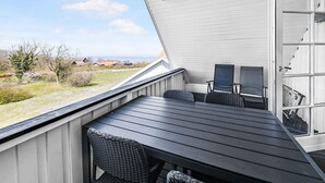 A covered outdoor seating area with a table and chairs, overlooking a grassy landscape and distant houses. - 5 Star Holiday Home in Allinge (Allinge)