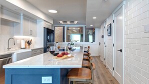 A modern kitchen with a large island, bar stools, and a view of the living area. - Ski Captain Molly 3 Bedroom Condo (Park City)
