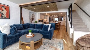A modern living room with a blue sectional sofa, a round coffee table, and a staircase leading to an upper level. - Ski Captain Molly 3 Bedroom Condo (Park City)