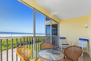 Un balcón con sillas de mimbre, una mesa de vidrio y vistas a la playa.