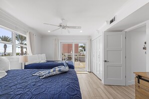 Un dormitorio con dos camas, ventilador de techo y vistas a palmeras fuera.
