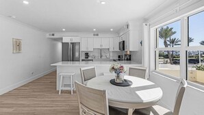 A modern kitchen with white cabinets, a central island, and a dining area with a round table and chairs. - Vacation Villas #131 2 Bedroom Condo (Fort Myers Beach)
