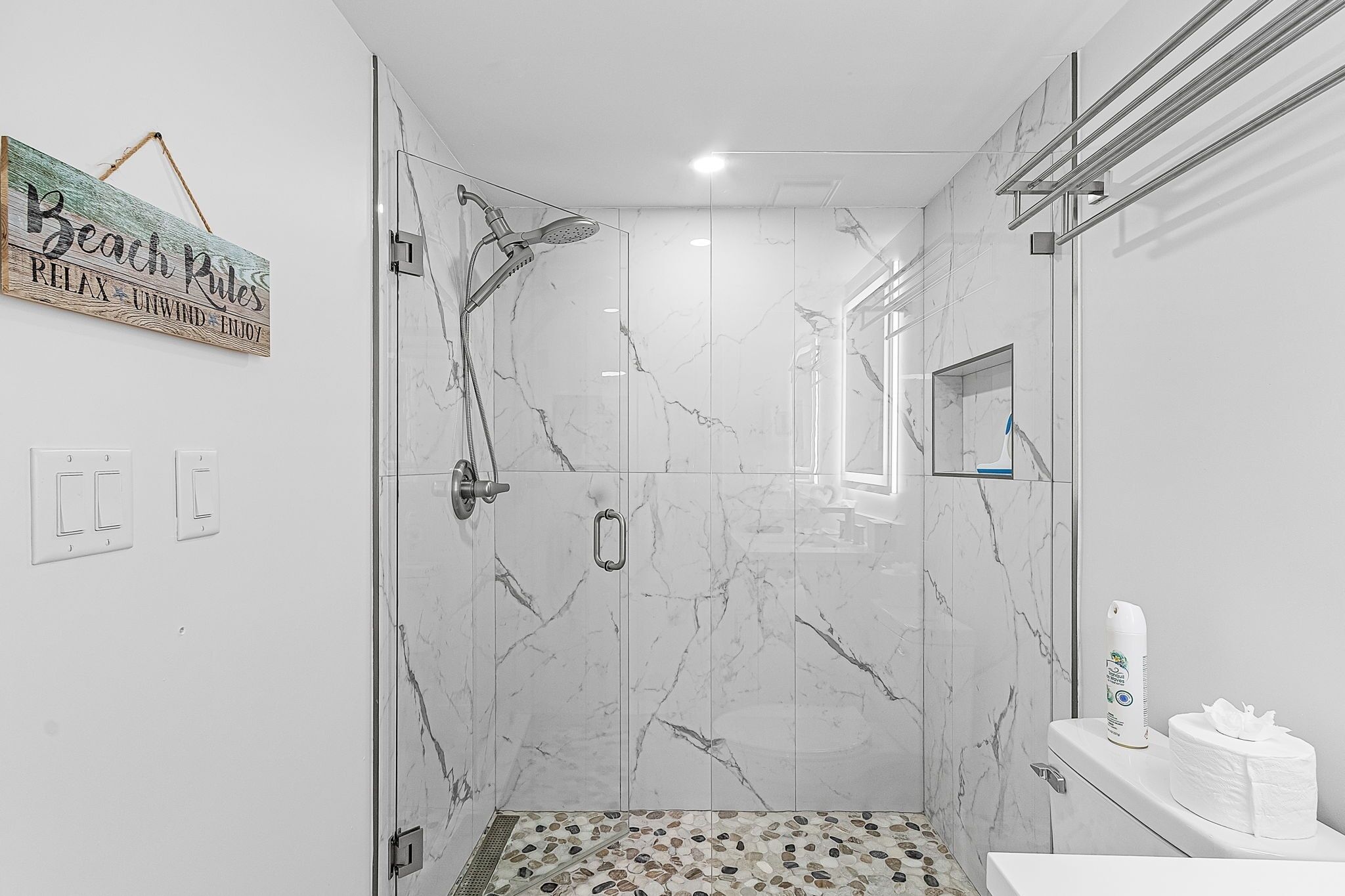 A modern bathroom with a glass-enclosed shower, marble walls, and a small sink area with a toilet.