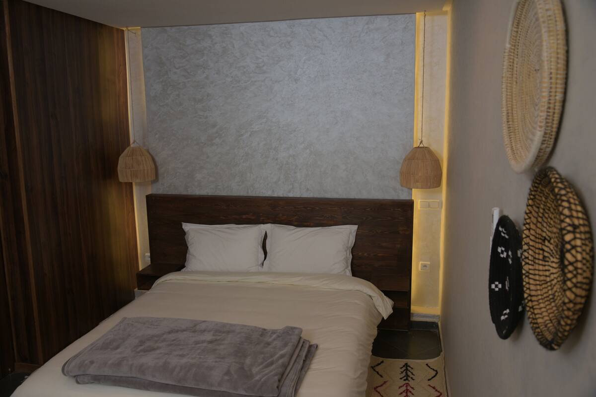 A neatly made bed with a gray blanket, wooden headboard, and two wall-mounted lamps.