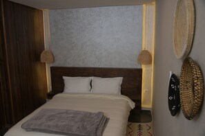 A neatly made bed with a gray blanket, wooden headboard, and two wall-mounted lamps. - Perle de Setti-Fadma (Sti Fadma)