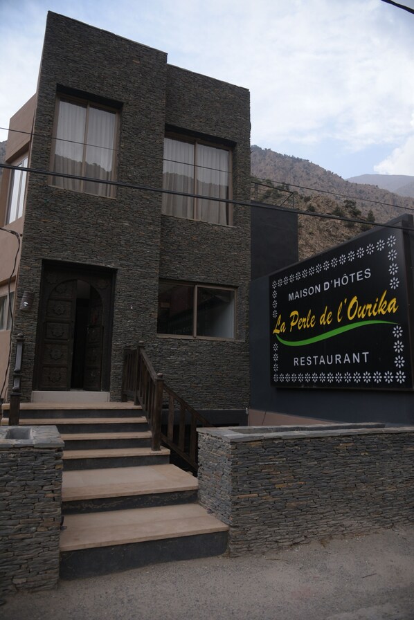 A modern building with a stone facade, a sign for Maison d'Hotes La Perle de l'Ourika Restaurant, and a staircase leading to the entrance. - Perle de Setti-Fadma (Sti Fadma)