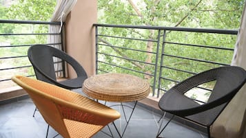 Un balcón con dos sillas de mimbre y una mesa redonda pequeña, con vistas a una zona verde exuberante.