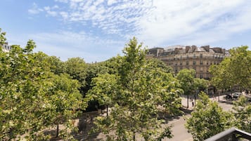Vista da rua com árvores, edifícios e céu claro.