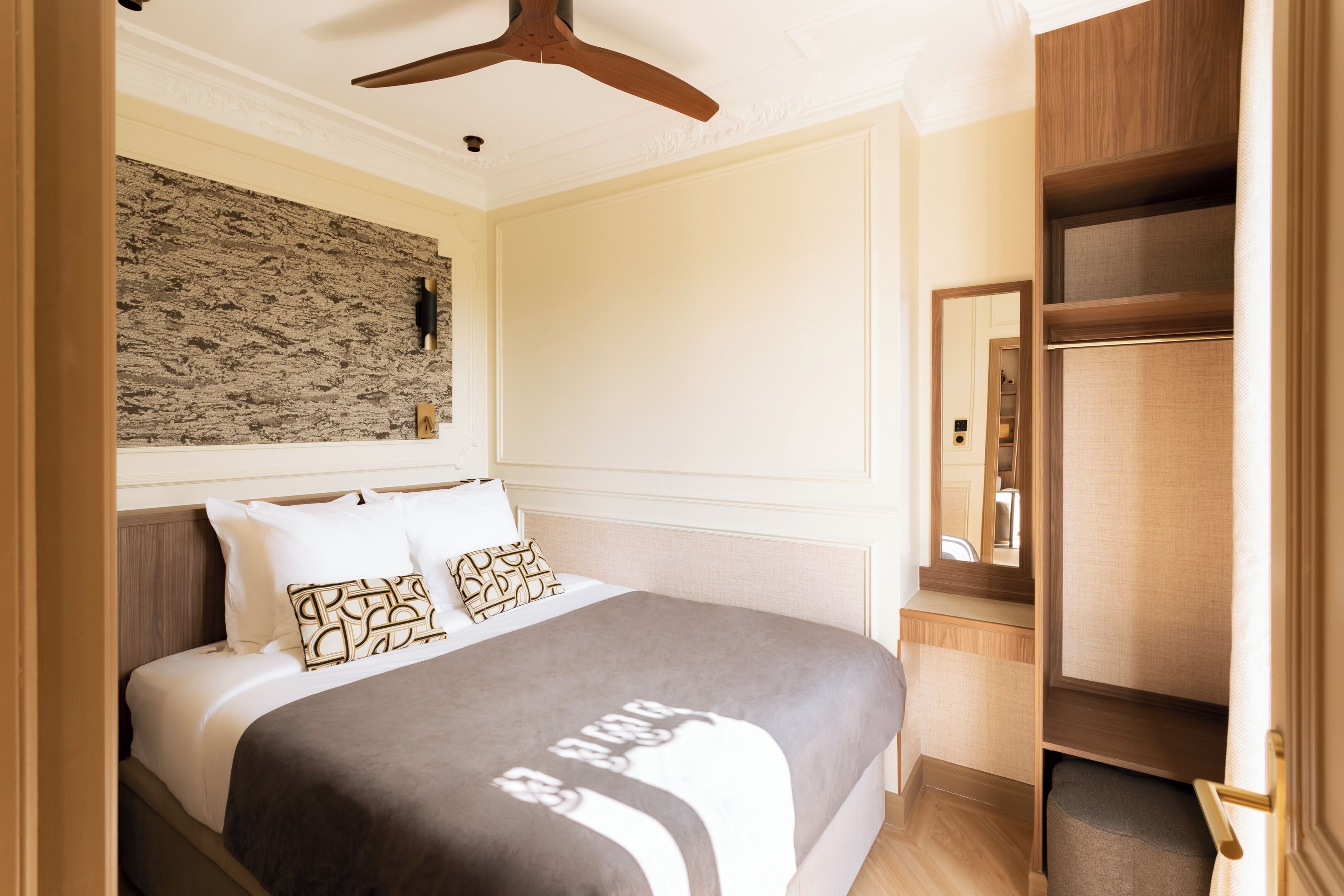 Ein Hotelzimmer mit einem Bett, einem hölzernen Deckenventilator, einer Wandleuchte und einem Spiegel.