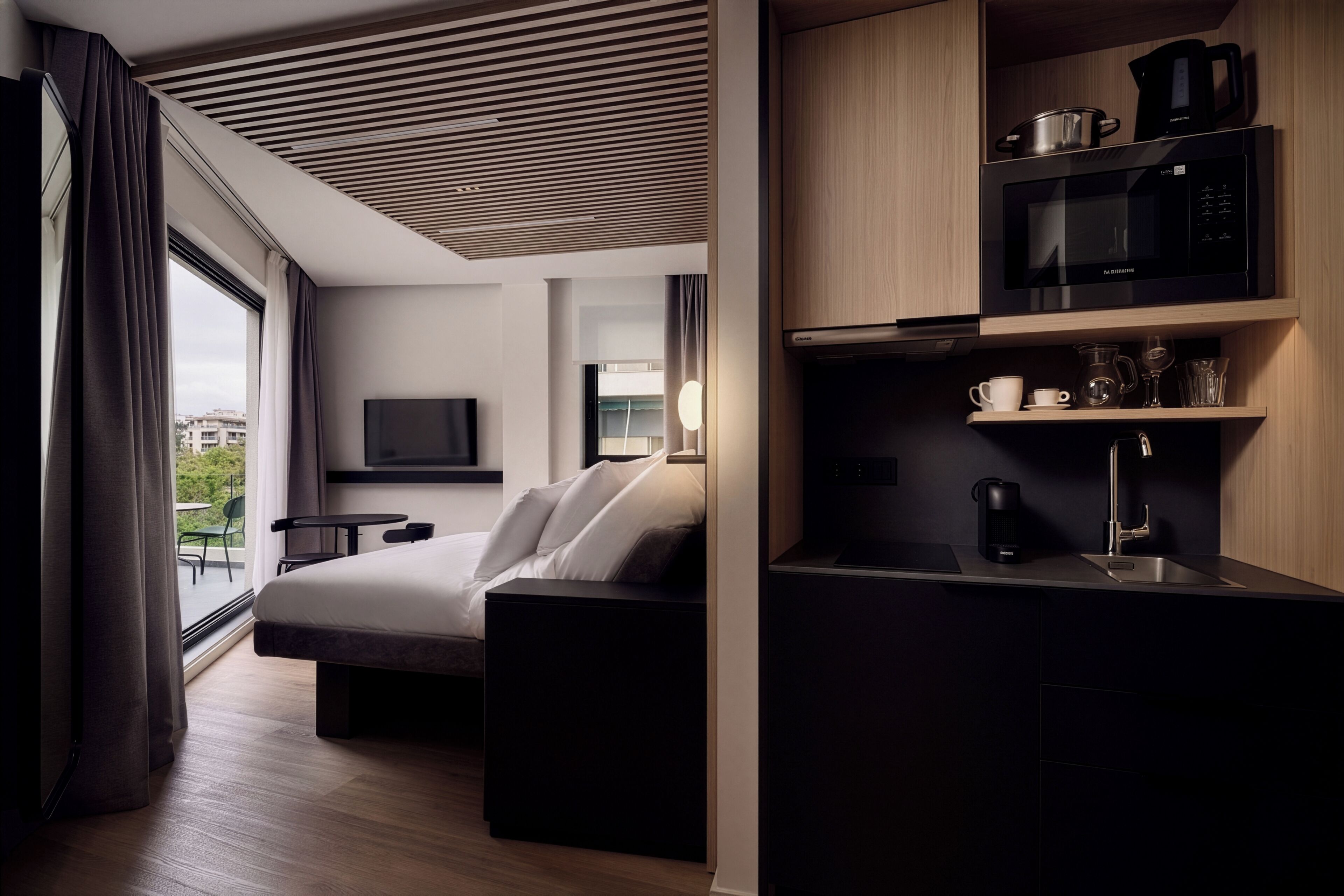 Una habitación de hotel moderna con cama, televisión, kitchenette y vistas al exterior.