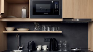 Ett modernt kök med inbyggd mikrovågsugn, kastruller i rostfritt stål, en kaffebryggare och en diskmaskin.
