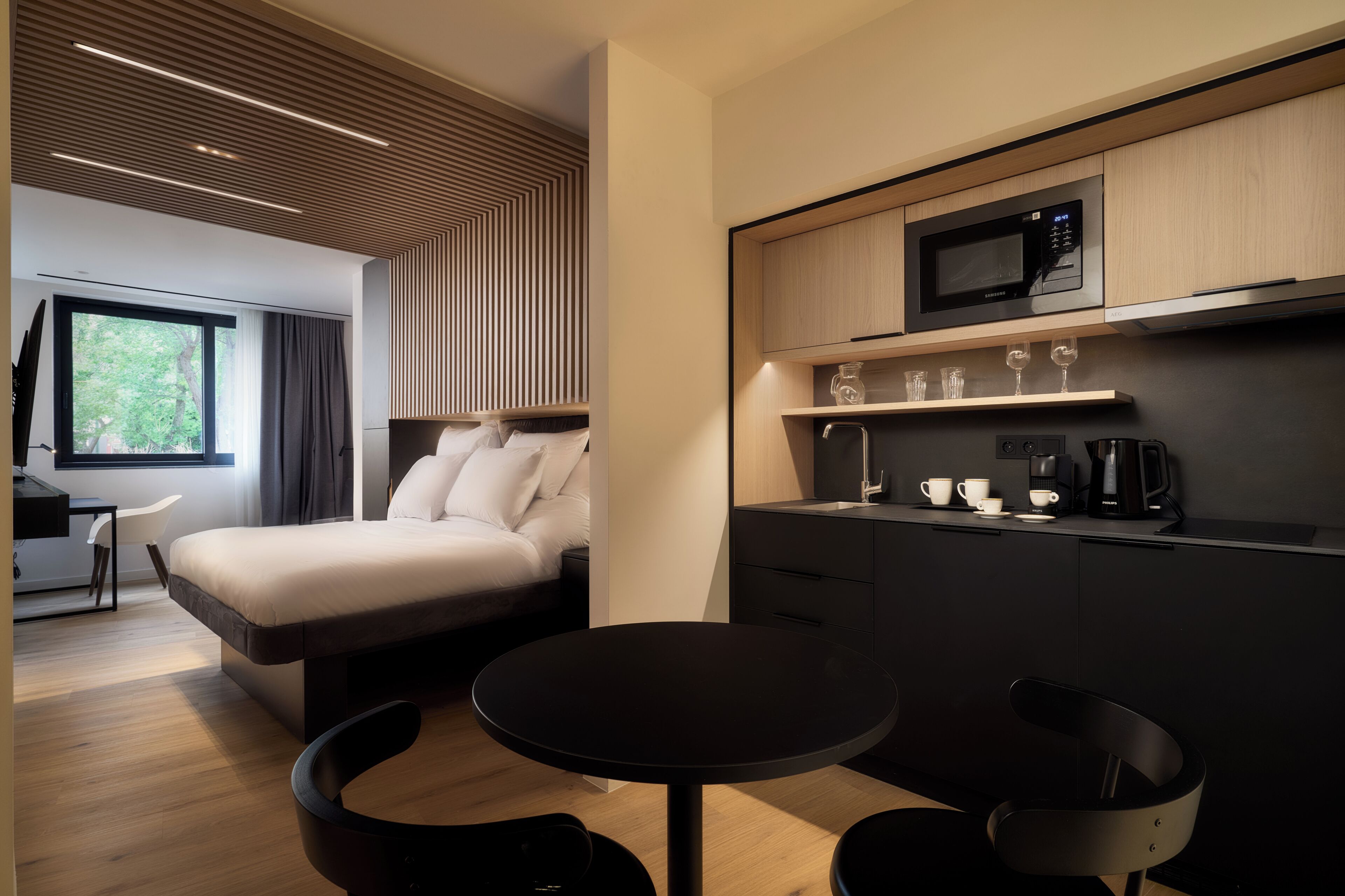 A modern hotel room with a bed, a small dining table, a microwave, and a coffee maker.