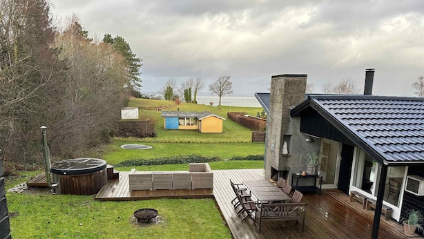 A backyard with a wooden deck, outdoor seating, a hot tub, and a small shed. - 5 Star Holiday Home in Knebel (Knebel)