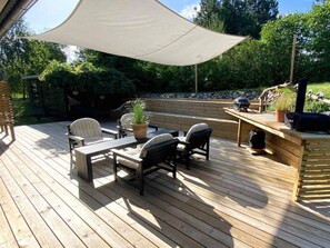 A wooden deck with outdoor furniture, a barbecue grill, and a large umbrella providing shade. - 5 Star Holiday Home in Knebel (Knebel)