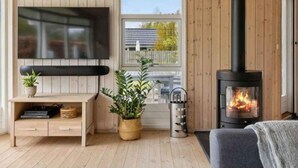A cozy cabin interior with a wooden interior, a TV mounted on the wall, a fireplace, and a window overlooking a house.
