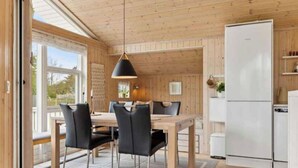 A modern kitchen with wooden walls and a large window, a dining area with a table and chairs, and a white refrigerator. - 5 Star Holiday Home in Eskebjerg (Eskebjerg)