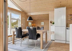A modern kitchen with wooden walls and a large window, a dining area with a table and chairs, and a white refrigerator. - 5 Star Holiday Home in Eskebjerg (Eskebjerg)
