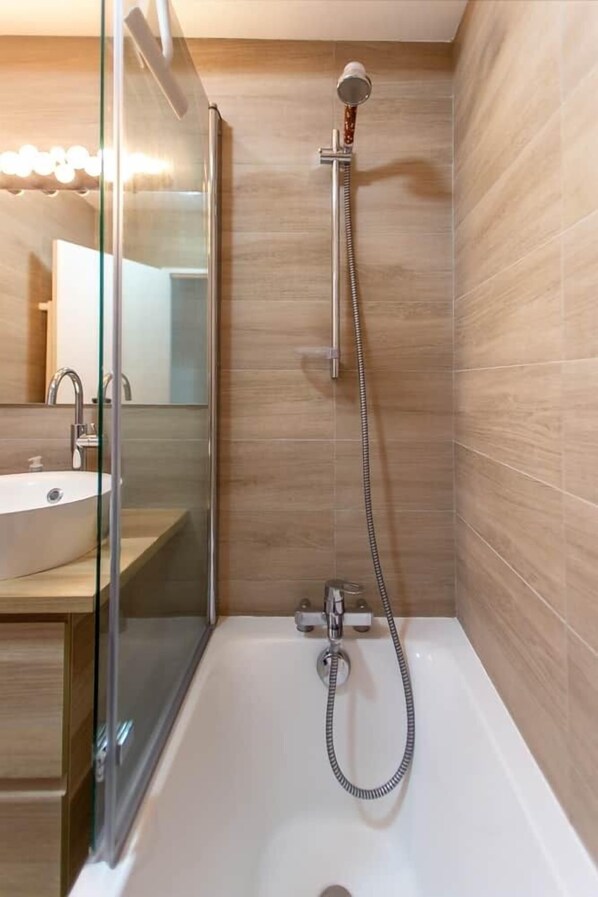 A bathroom with a glass-enclosed shower, a white bathtub, and a wooden vanity with a mirror.