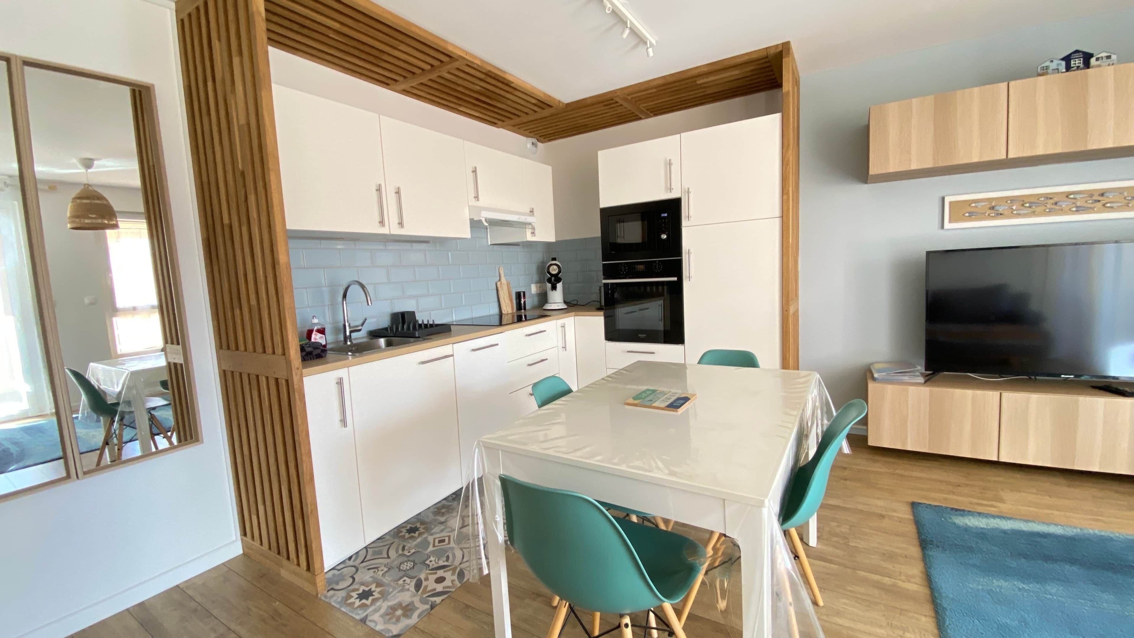 A modern kitchen with white cabinets, a microwave, and a stove. There is a dining table with chairs and a TV on a stand.
