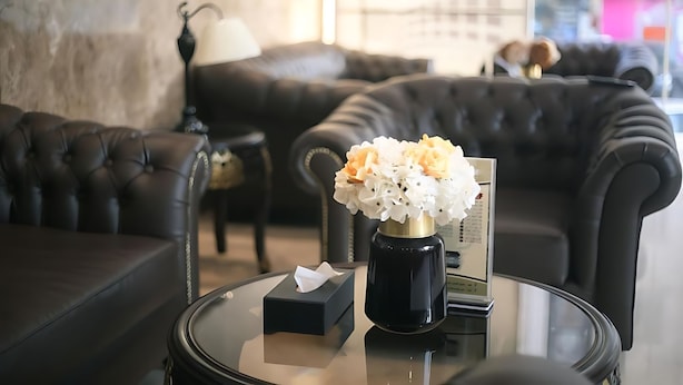 Un salon moderne avec un canapé en cuir, une table basse en verre ornée d’une boîte à mouchoirs et d’un vase, et une lampe.