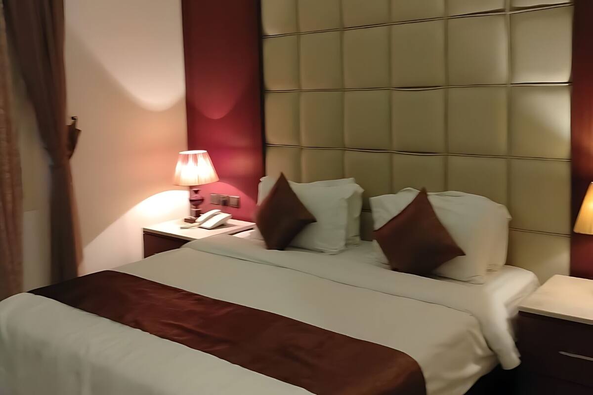 Ein Hotelzimmer mit einem großen Bett, einem Nachttisch mit Lampe und einem gepolsterten Kopfteil.