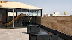 Une terrasse sur le toit dotée d’une structure vitrée, d’un toboggan et de coins salon extérieurs.