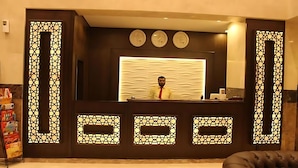 Un comptoir d'accueil orné d'un motif décoratif, trois horloges au-dessus, et une personne debout derrière.