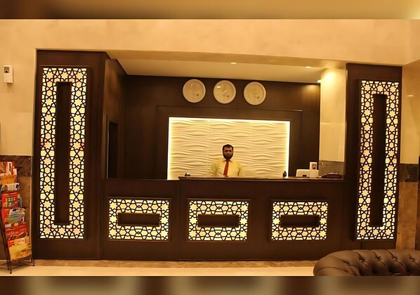 A reception desk with a patterned design, three clocks above it, and a person standing behind it.