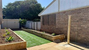 A backyard with a brick wall, a wooden fence, and a grassy area. - Spacious Villa with Comfortable Beds (Rangeway)
