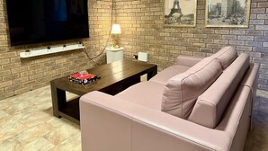 A living room with a brick wall, a flat-screen TV, a sofa, a coffee table, and two framed pictures of the Eiffel Tower. - Spacious Villa with Comfortable Beds (Rangeway)