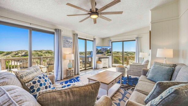 A spacious living area with a ceiling fan, large windows, and a view of the beach. - Oceanfront Home in Avon with Hot Tub and Stunning Views (Avon)