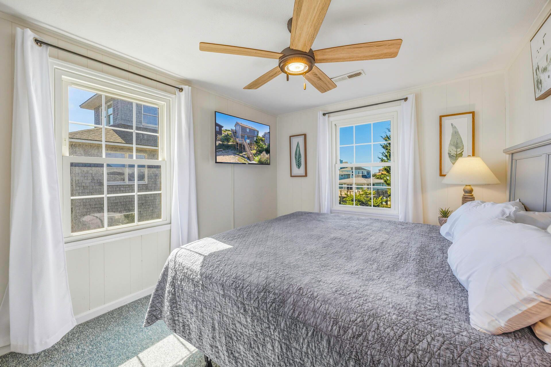 A bedroom with a bed, a ceiling fan, and large windows.