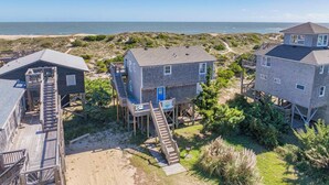 A beachfront property with multiple houses connected by wooden walkways, offering views of the ocean. - Oceanfront Home in Avon with Hot Tub and Stunning Views (Avon)