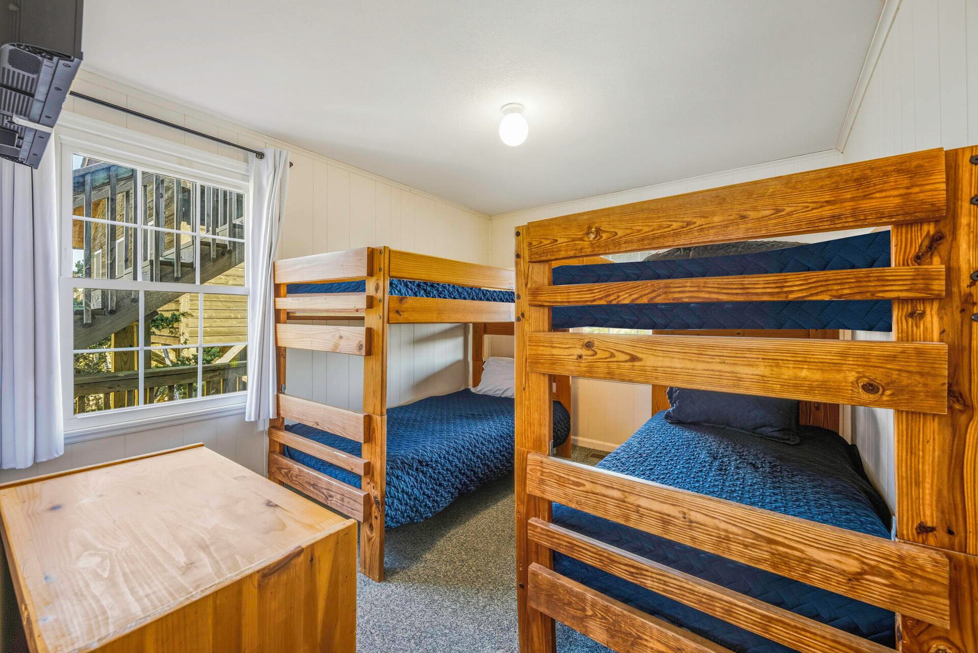 A bunk bed room with a wooden table and a window with curtains.