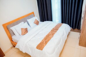 A neatly made bed with a wooden headboard, a brown accent pillow, and a white comforter. - THELIGHT SUITES KIGALI (Kigali)