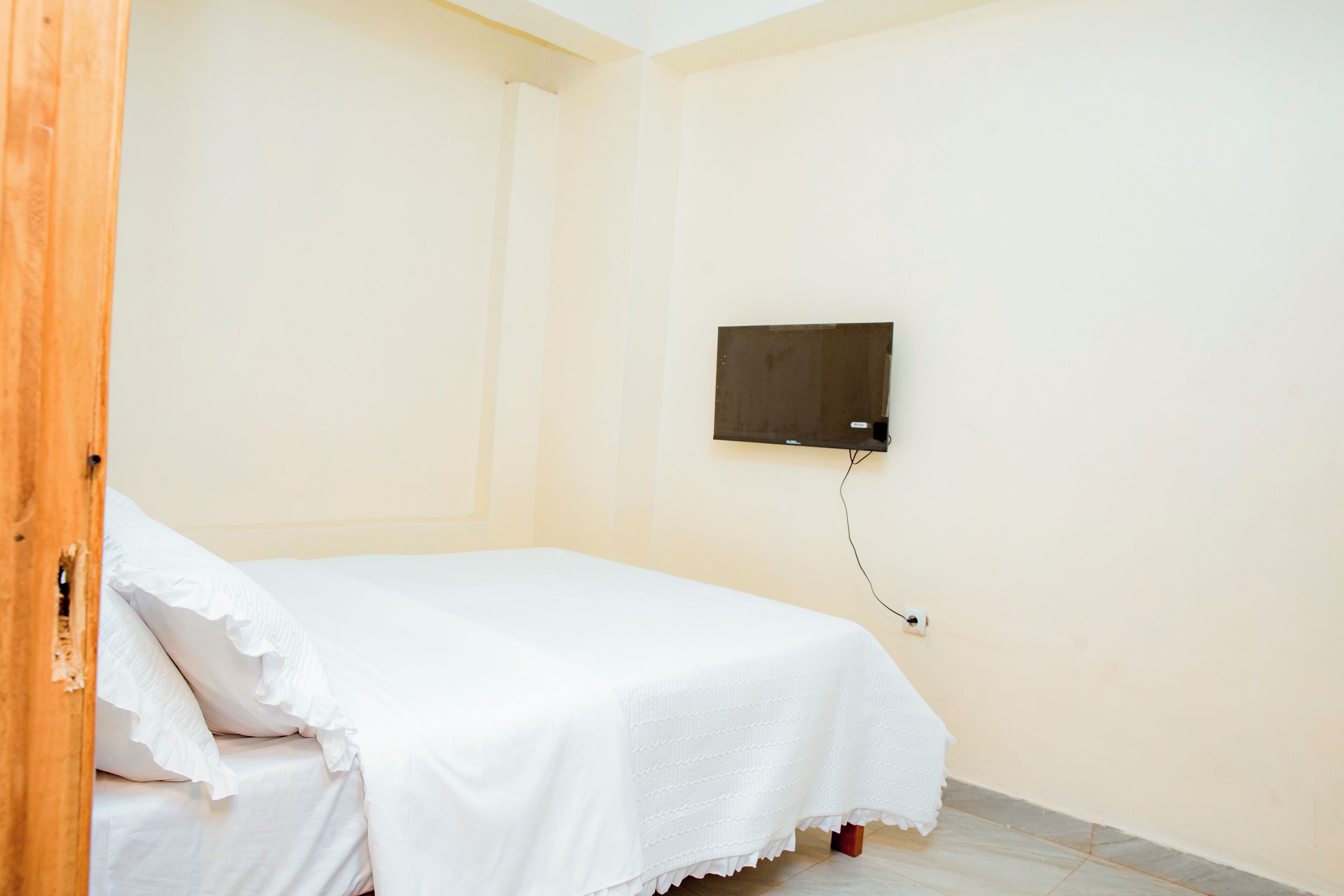 Une chambre avec un lit, un téléviseur fixé au mur et une porte en bois.