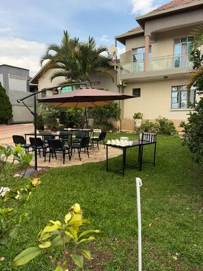 A patio with a table and chairs, a large umbrella, and a small table with dishes. - THELIGHT SUITES KIGALI (Kigali)