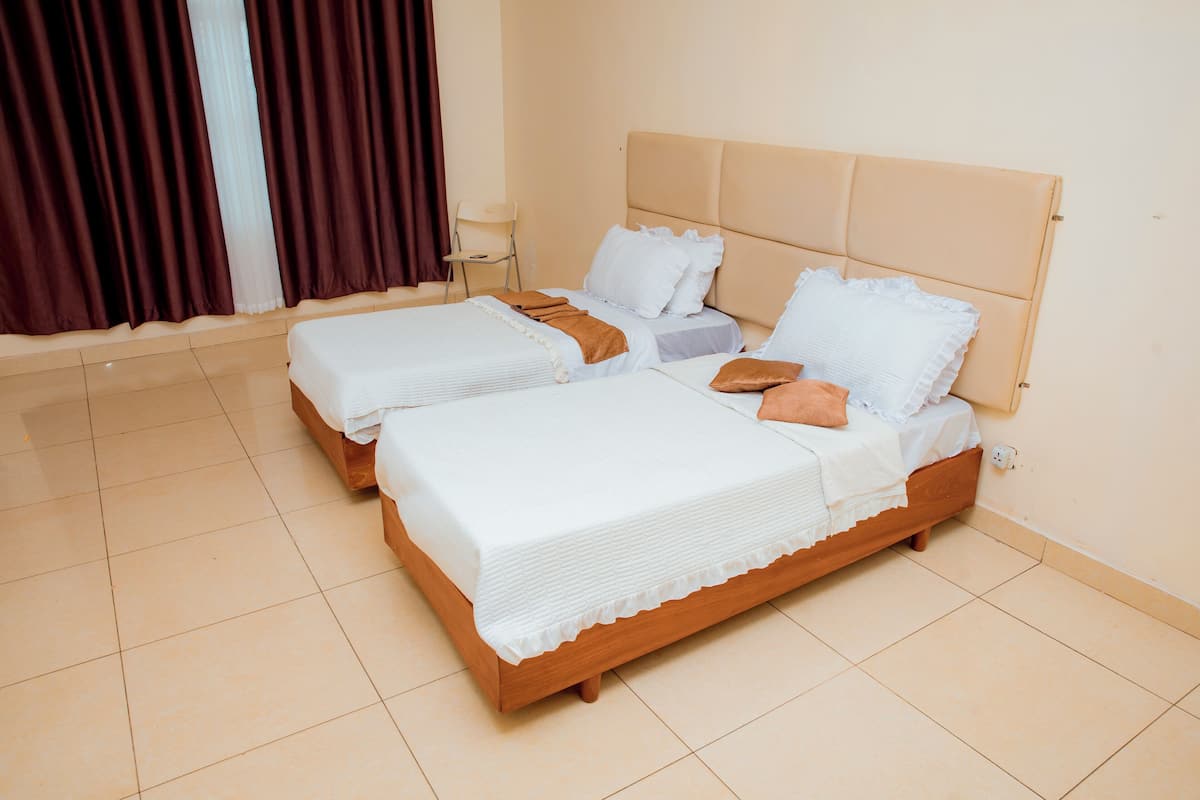 A hotel room with two beds, a chair, and a window with curtains.