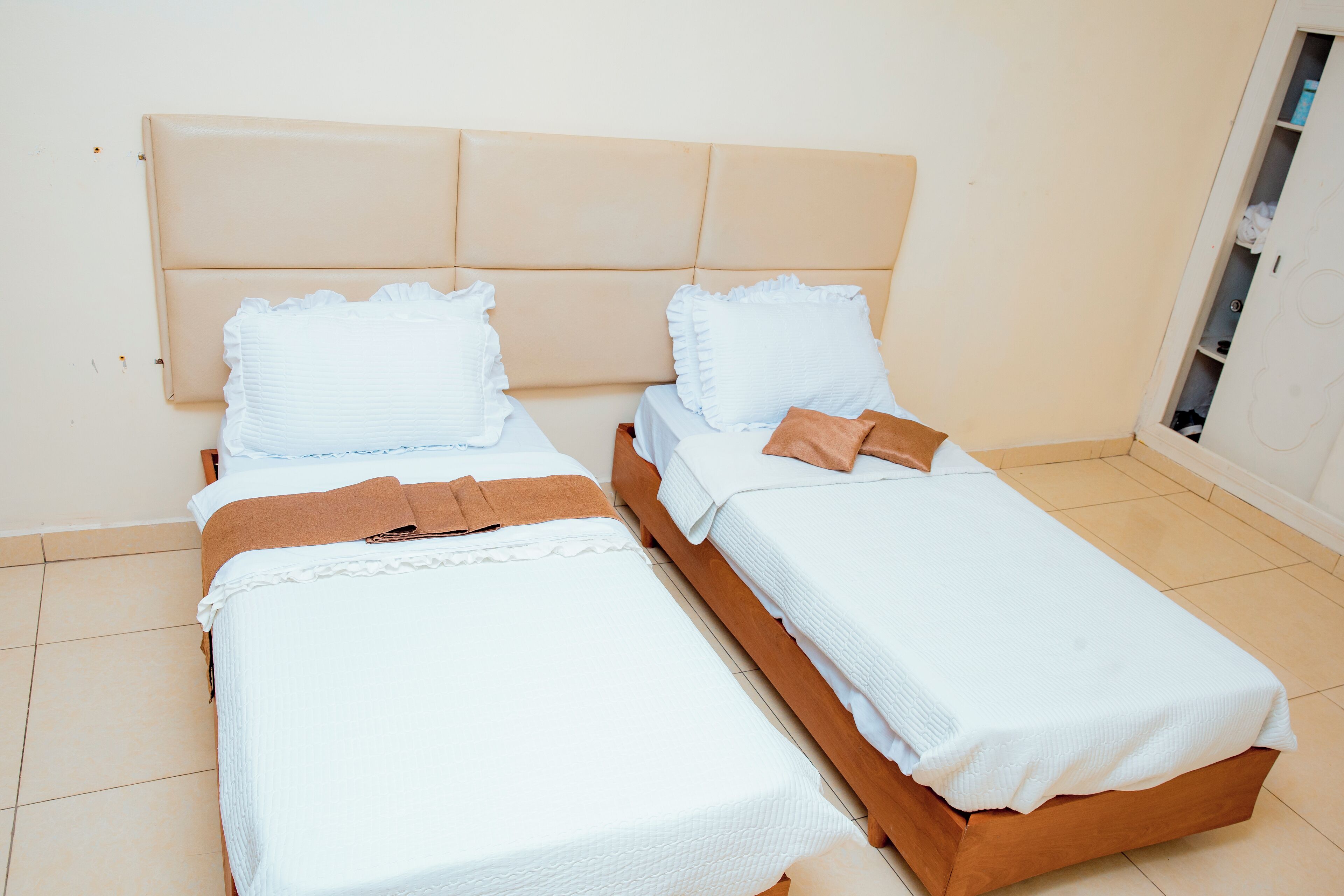 A room with two single beds, each with a headboard, white bedding, and brown towels.