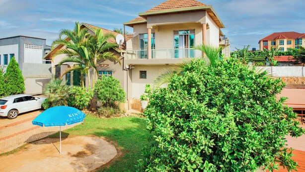 A two-story house with a balcony, a white car parked in the driveway, and a blue umbrella. - THELIGHT SUITES KIGALI (Kigali)