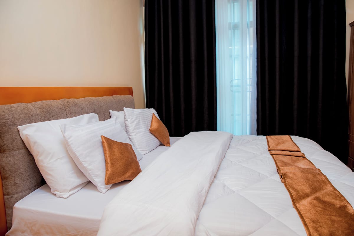 A hotel room with a bed, pillows, a headboard, and a window with curtains.