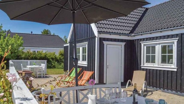 En udendørs patio med et spisebord, et hvidt hegn og en sort parasol.